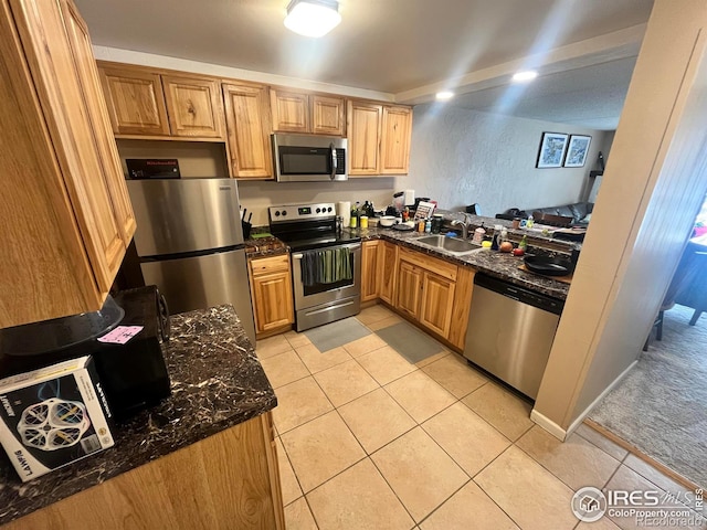 kitchen with light tile patterned floors, stainless steel appliances, dark stone counters, and a sink