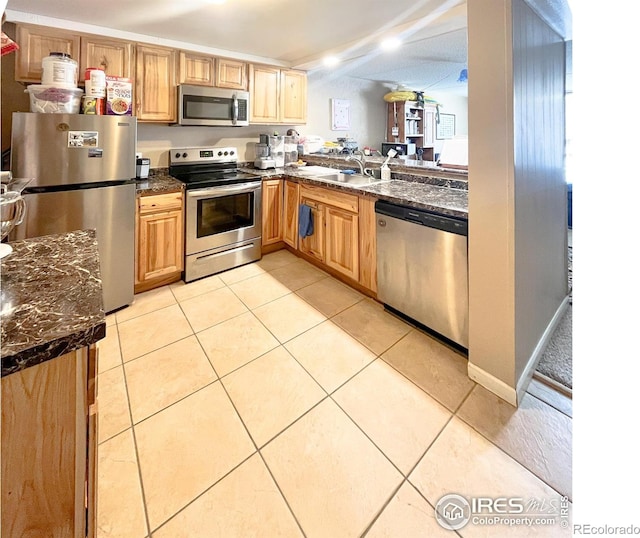 kitchen with light tile patterned floors, dark stone countertops, appliances with stainless steel finishes, and a sink