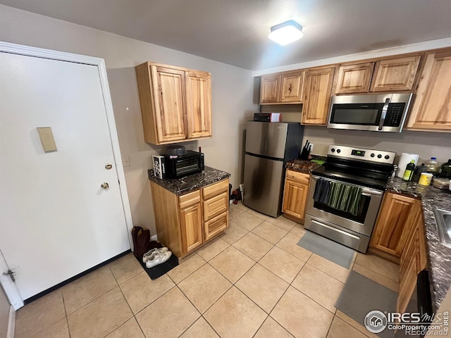 kitchen featuring light tile patterned floors, stainless steel appliances, and dark stone countertops