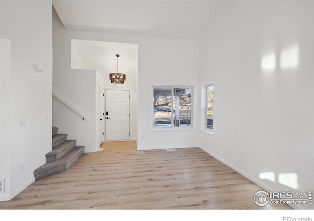 foyer entrance featuring a chandelier, a towering ceiling, baseboards, stairs, and light wood-type flooring