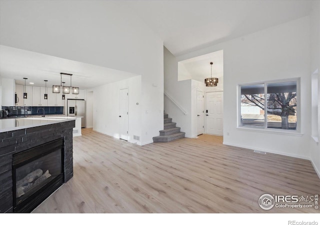 living area with light wood finished floors, visible vents, baseboards, a glass covered fireplace, and stairway