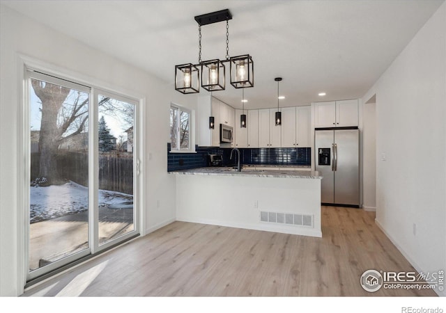 kitchen with light stone counters, visible vents, appliances with stainless steel finishes, white cabinetry, and a peninsula