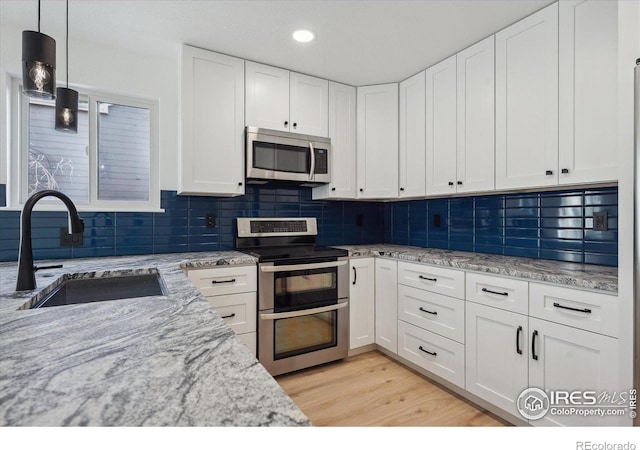 kitchen featuring hanging light fixtures, light stone countertops, stainless steel appliances, white cabinetry, and a sink