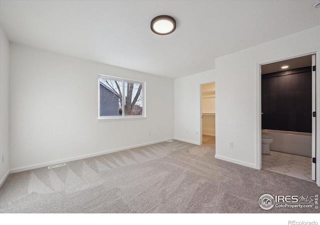 unfurnished bedroom featuring connected bathroom, light colored carpet, baseboards, a closet, and a walk in closet