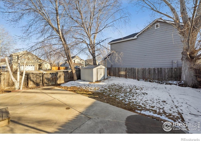 snow covered property with a shed, a patio, a fenced backyard, and an outdoor structure