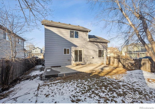 snow covered rear of property featuring a fenced backyard and a patio