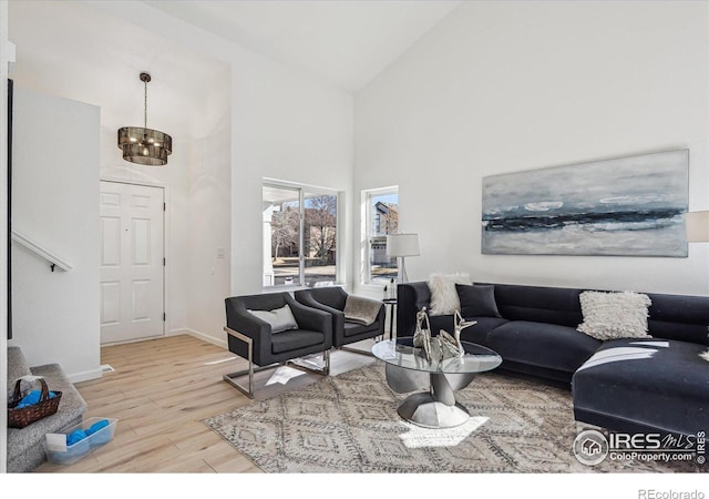 living area featuring baseboards, high vaulted ceiling, wood finished floors, and an inviting chandelier