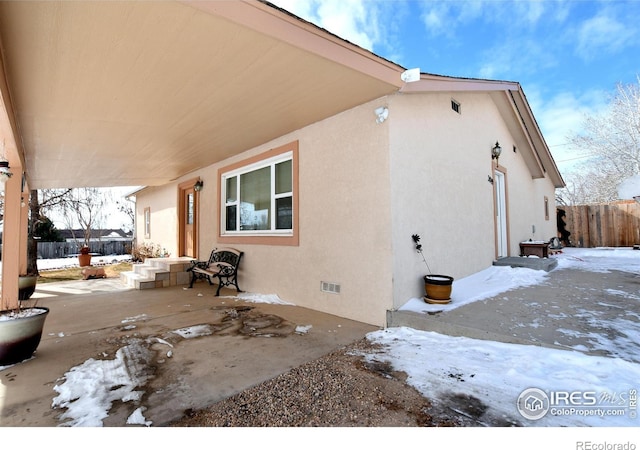 view of snowy exterior with fence and stucco siding