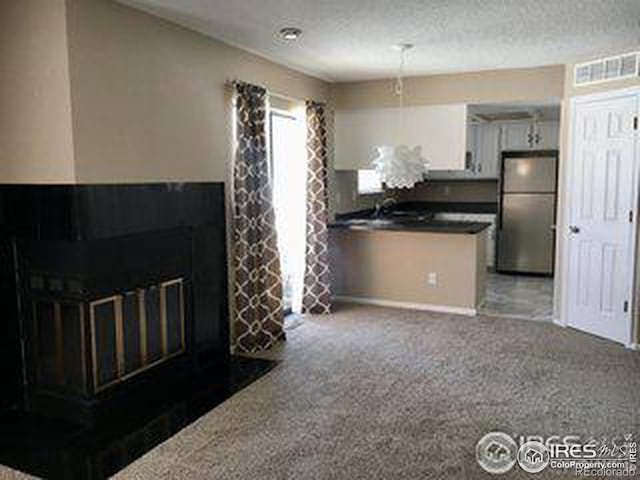 kitchen with a fireplace with flush hearth, visible vents, carpet flooring, white cabinetry, and freestanding refrigerator