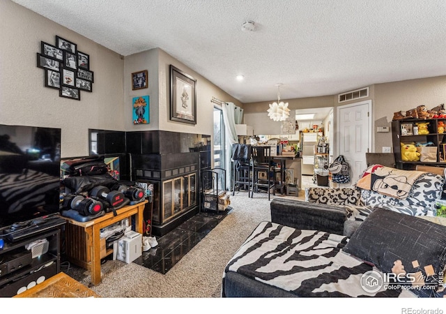 living room with visible vents, a chandelier, a tiled fireplace, a textured ceiling, and dark carpet