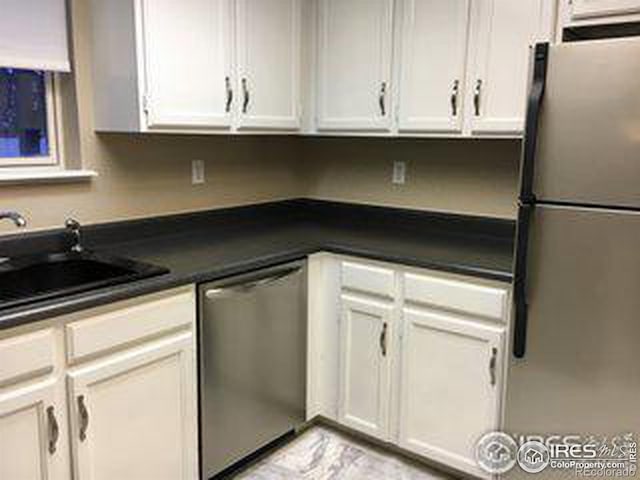 kitchen with stainless steel appliances, dark countertops, white cabinetry, and a sink