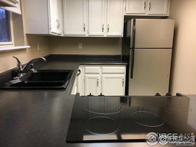 kitchen featuring freestanding refrigerator, white cabinetry, a sink, and dark countertops