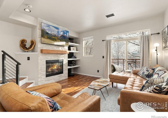 living room with visible vents, baseboards, wood finished floors, stairs, and a stone fireplace