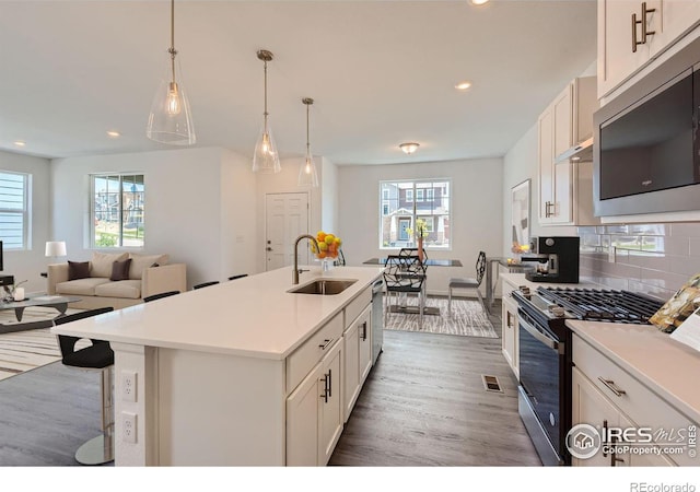 kitchen featuring pendant lighting, light countertops, appliances with stainless steel finishes, a kitchen island with sink, and a sink