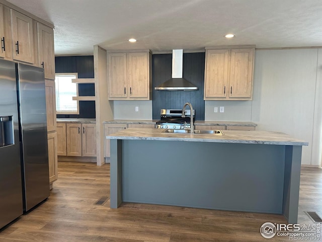 kitchen featuring an island with sink, appliances with stainless steel finishes, wood finished floors, wall chimney range hood, and a sink