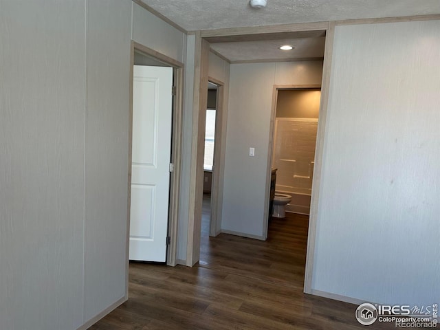 corridor featuring dark wood-type flooring, a textured ceiling, and baseboards