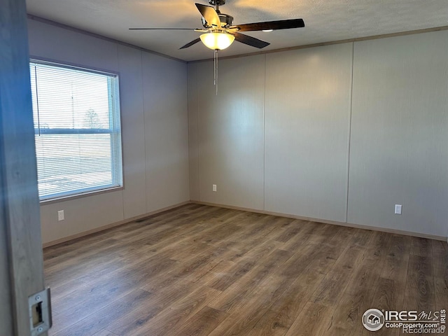 empty room featuring ceiling fan, ornamental molding, a decorative wall, and wood finished floors