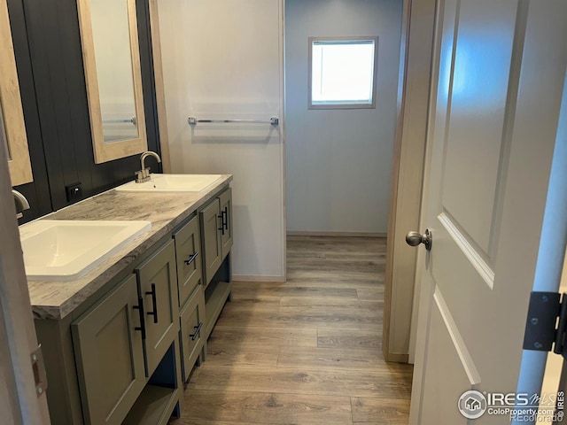 full bath with double vanity, baseboards, a sink, and wood finished floors