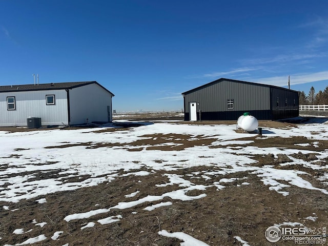 snow covered structure with cooling unit, a pole building, and an outdoor structure