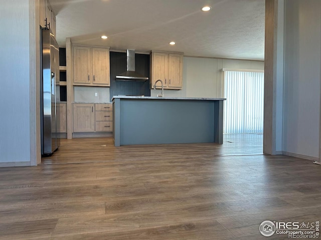 kitchen with stainless steel fridge, wood finished floors, light countertops, wall chimney range hood, and recessed lighting