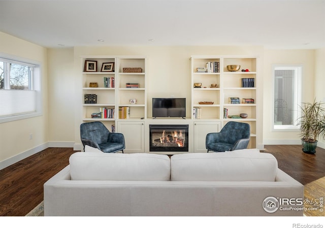 living room featuring dark wood-type flooring, a glass covered fireplace, and baseboards