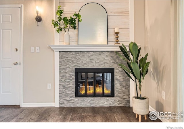 details featuring baseboards, a tiled fireplace, and wood finished floors