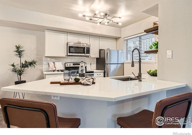 kitchen featuring tasteful backsplash, a peninsula, stainless steel appliances, white cabinetry, and a sink