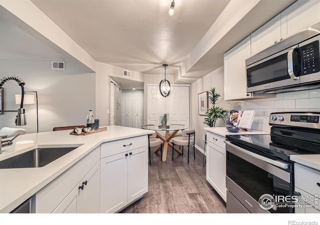 kitchen with light countertops, hanging light fixtures, appliances with stainless steel finishes, white cabinetry, and a sink