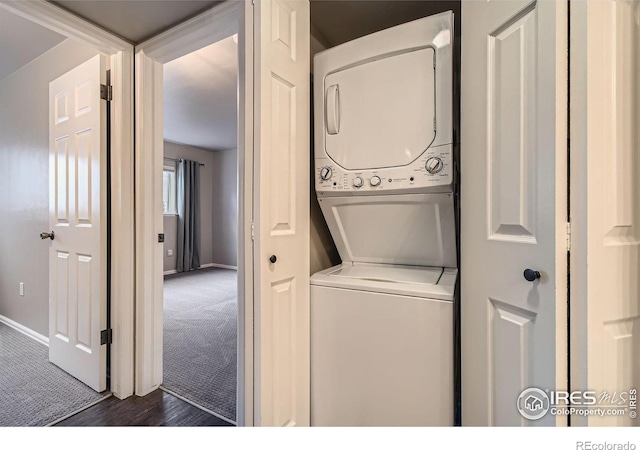 clothes washing area featuring laundry area, baseboards, dark colored carpet, and stacked washer / dryer