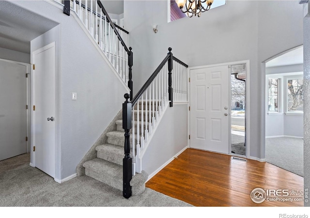 carpeted foyer featuring visible vents, stairway, a towering ceiling, wood finished floors, and a chandelier