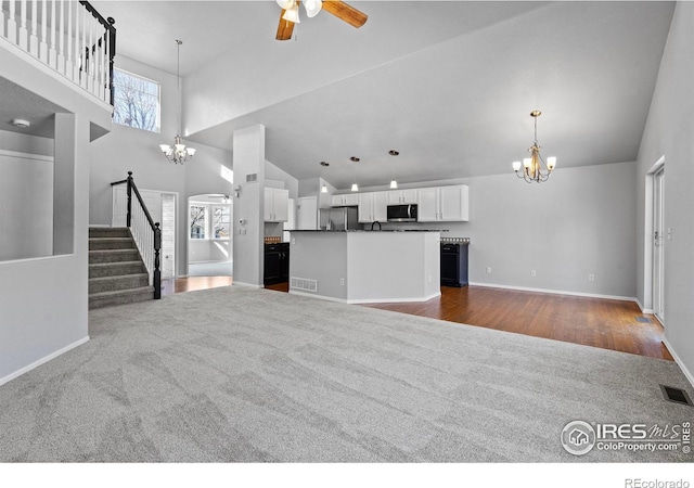 unfurnished living room with visible vents, stairway, dark colored carpet, high vaulted ceiling, and ceiling fan with notable chandelier