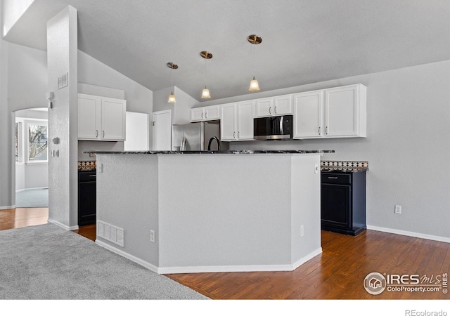 kitchen with white cabinets, dark countertops, a kitchen island with sink, stainless steel appliances, and pendant lighting