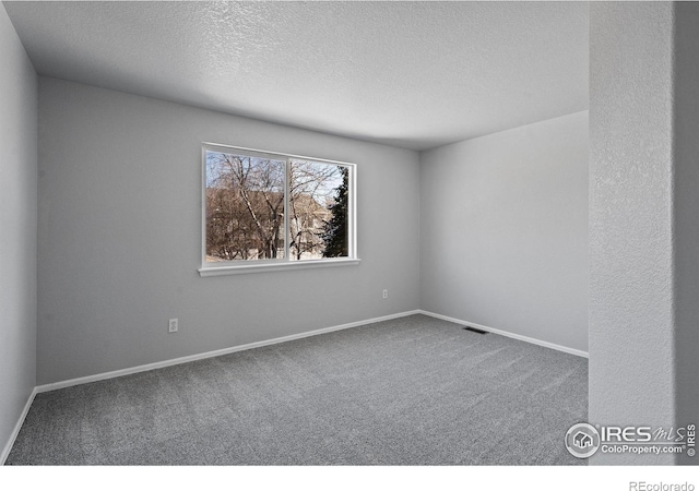 carpeted empty room featuring baseboards, visible vents, and a textured ceiling