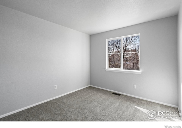 empty room with carpet floors, visible vents, a textured ceiling, and baseboards