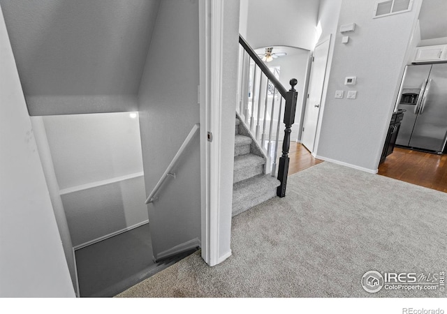 staircase featuring wood finished floors, carpet flooring, baseboards, visible vents, and a ceiling fan