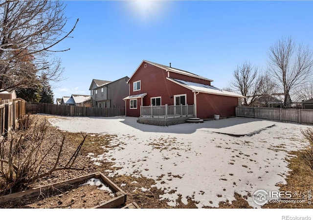 snow covered house with a fenced backyard and a wooden deck