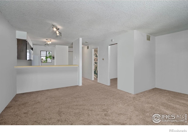 spare room featuring light carpet, a textured ceiling, and visible vents