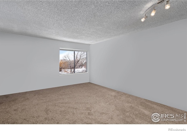 carpeted empty room with rail lighting and a textured ceiling