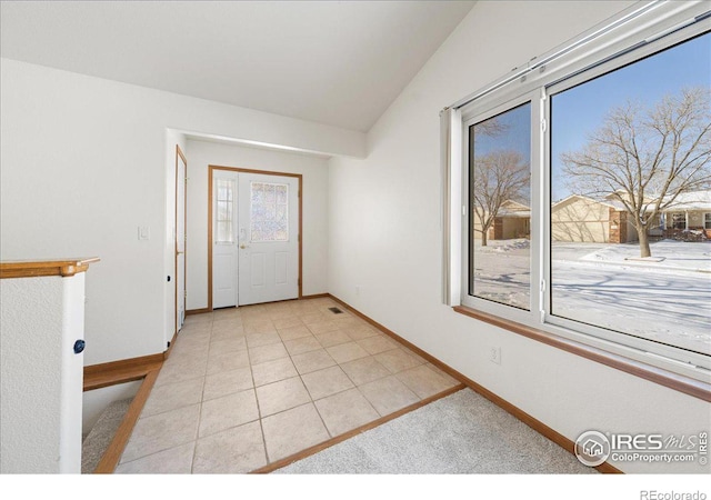 empty room with vaulted ceiling, light tile patterned flooring, and baseboards