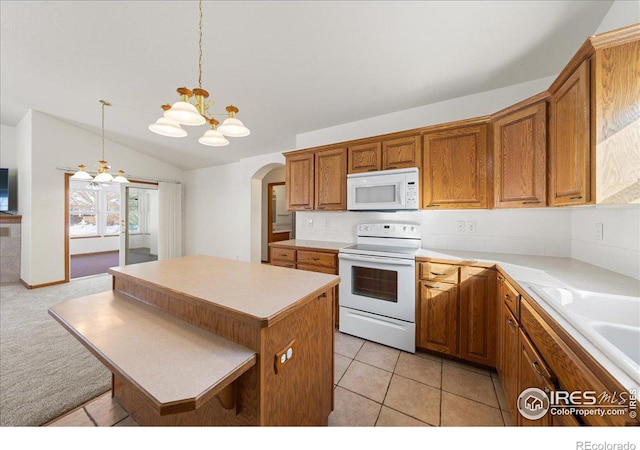 kitchen featuring white appliances, brown cabinetry, a kitchen island, decorative light fixtures, and light countertops