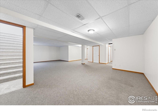 finished basement featuring carpet, visible vents, a drop ceiling, and baseboards