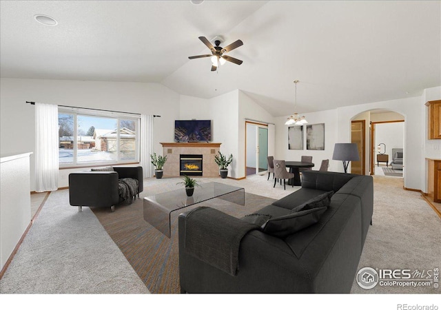 living area featuring arched walkways, vaulted ceiling, a tiled fireplace, and light colored carpet