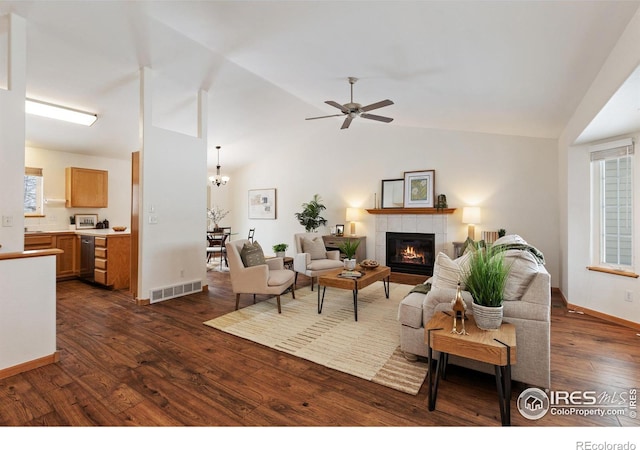 living area with dark wood-style flooring, visible vents, vaulted ceiling, and a tiled fireplace