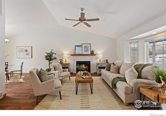 living area with lofted ceiling, a tile fireplace, wood finished floors, visible vents, and a ceiling fan