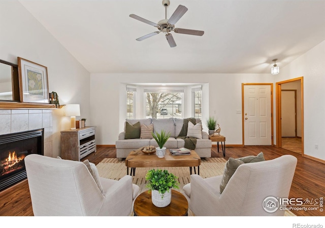 living room featuring dark wood-style floors, vaulted ceiling, ceiling fan, a tile fireplace, and baseboards