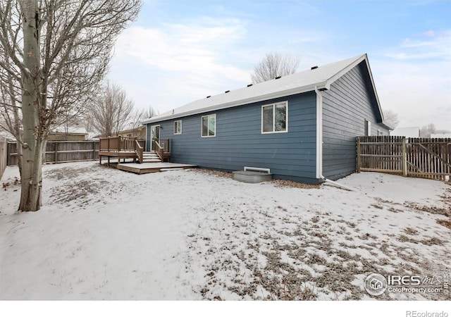 snow covered rear of property with a deck and fence