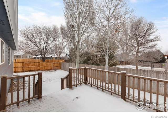 snow covered deck with a fenced backyard