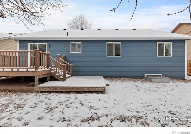 snow covered back of property with a wooden deck