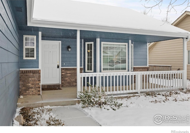 snow covered property entrance featuring covered porch and brick siding