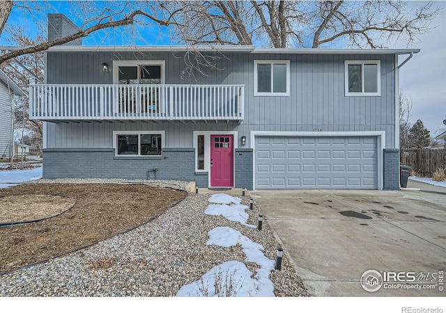 view of front of home with an attached garage, a balcony, brick siding, driveway, and a chimney